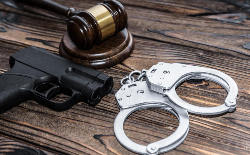 Gavel, handgun, and handcuffs on wooden table representing unlawful carry defense in criminal law cases.