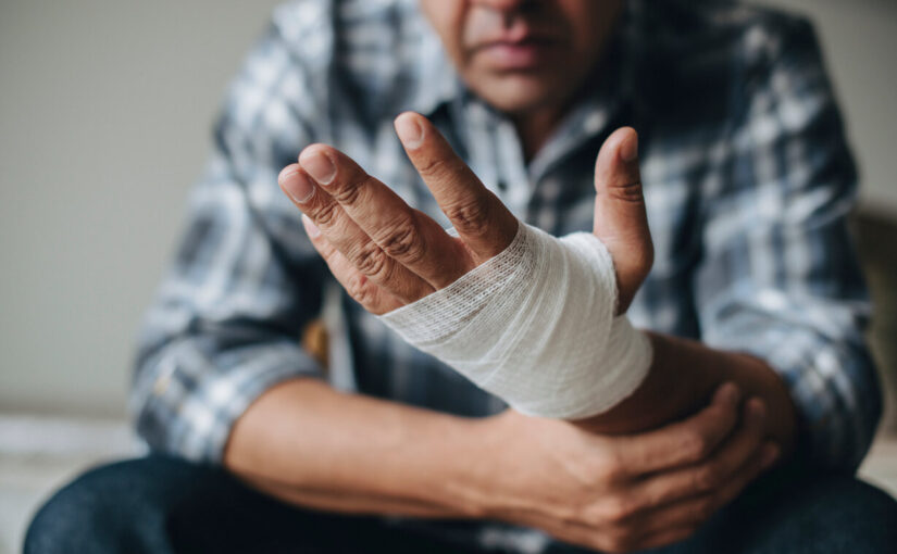 Man with a bandaged hand sitting indoors, looking at his injury—illustrating injury from a defective product.