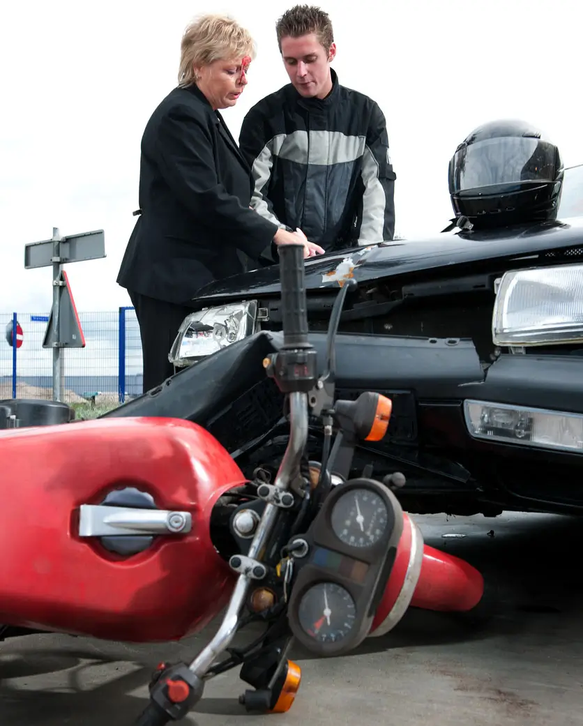 Motorcyclist and driver calmly assessing damage after a motorcycle‑vs‑car collision on a suburban roadway.