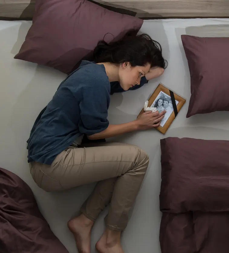 Grieving woman lying on bed holding framed family photo after loved one’s wrongful death