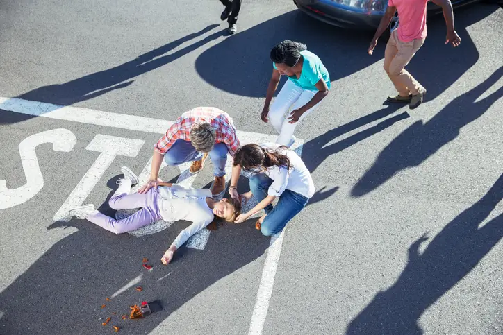 Bystanders helping injured pedestrian lying in crosswalk after car crash